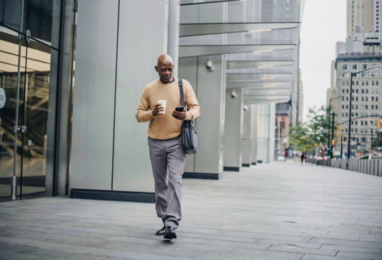KONE - Man walking outside office building holding coffee cup and a smartphone.