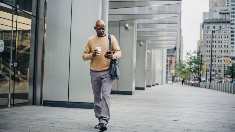 KONE - Man walking outside office building holding coffee cup and a smartphone.