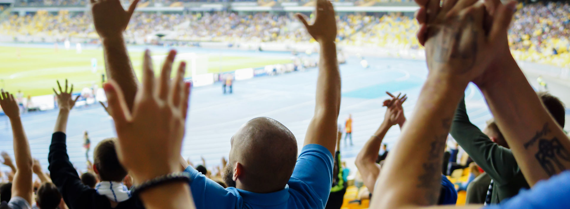 Back view of football fans cheering at a full stadium.