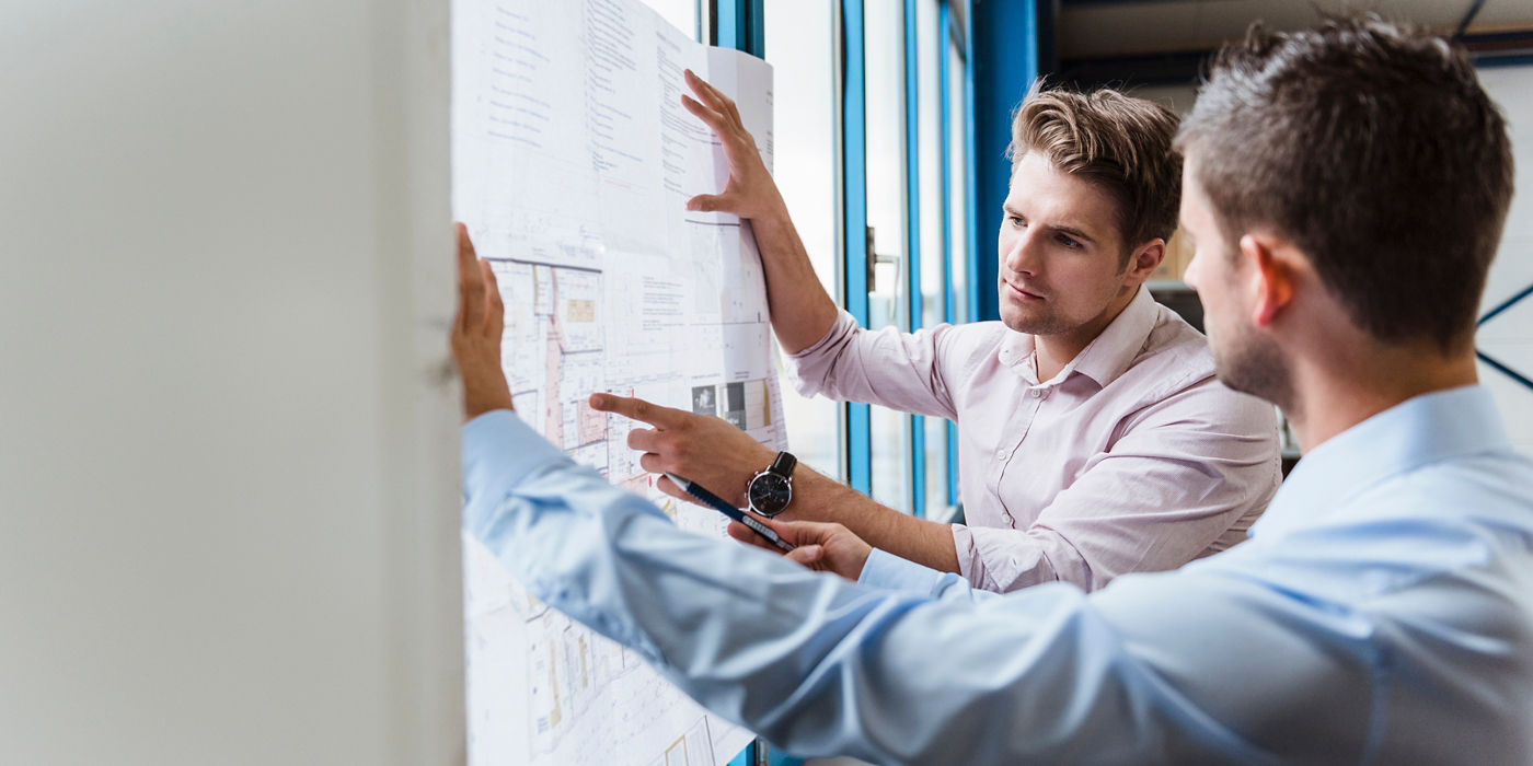 Two men having planning discussion while looking at a blueprint.