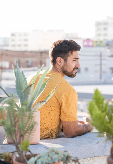 Man in yellow T-shirt sitting among plants on a urban roof garden in the sunshine.