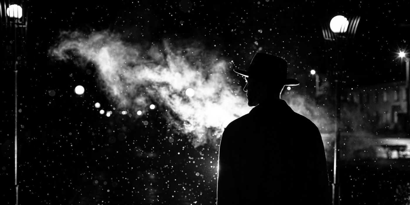 Dark silhouette of a man in a hat in the rain on a night street in a city.
