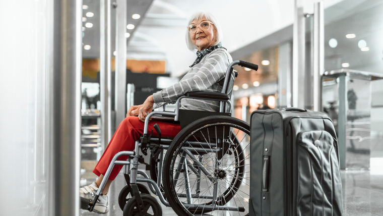 Mature woman with laptop and luggage sitting in wheelchair at airport.