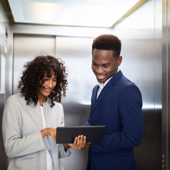 Two people standing in elevator checking something on tablet.