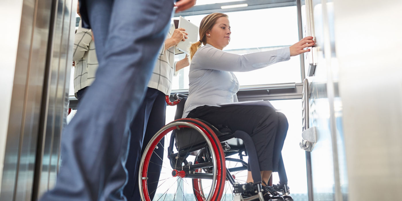Una mujer en silla de ruedas pulsa el botón del elevador por la inclusión y la accesibilidad