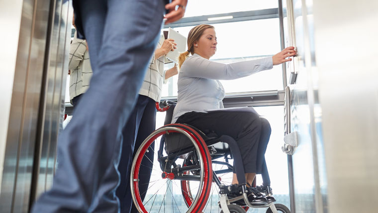 Una mujer en silla de ruedas pulsa el botón del elevador por la inclusión y la accesibilidad