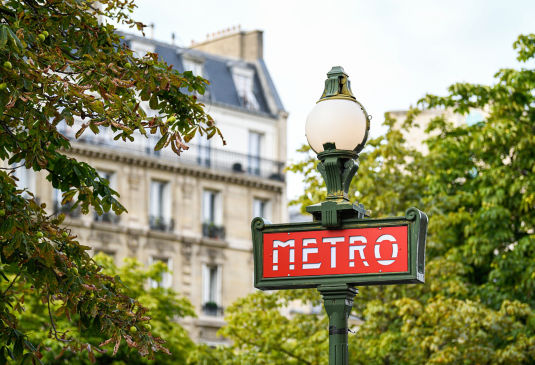 Paris metro sign with trees and apartment block in the background.