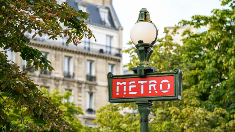 Paris metro sign with trees and apartment block in the background.