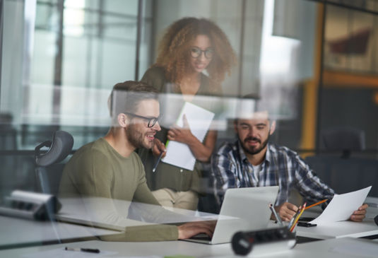 deux hommes et une femme regardant un ecran d'ordinateur au bureau.