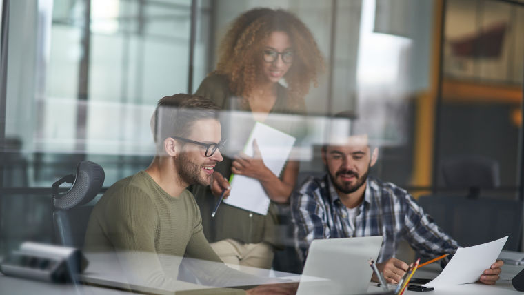 Two men and a woman on a desk looking at the computer