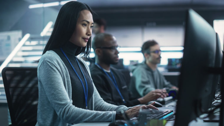 Three people side by side typing on computers in office.