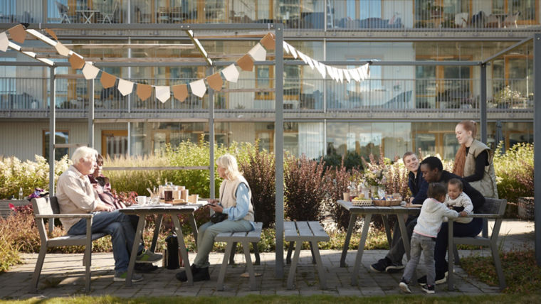 People gathered around tables in an apartment house backyard.