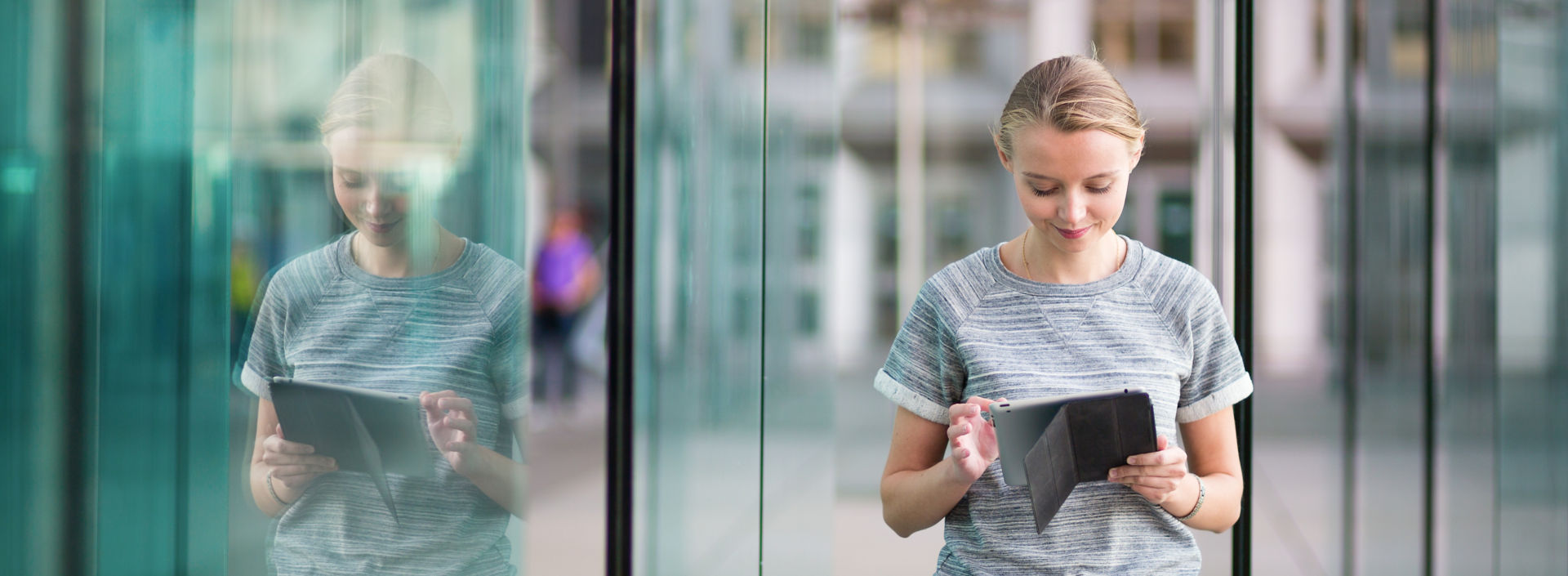 Smiling young woman using tablet in modern glass office environment.