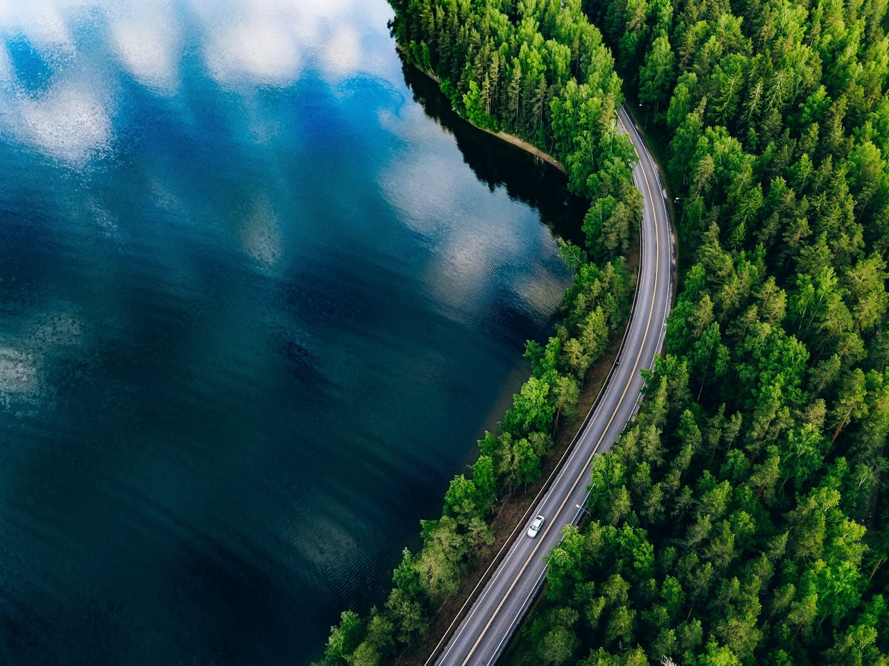 Aerial view of road between green summer forest and blue lake in Finland