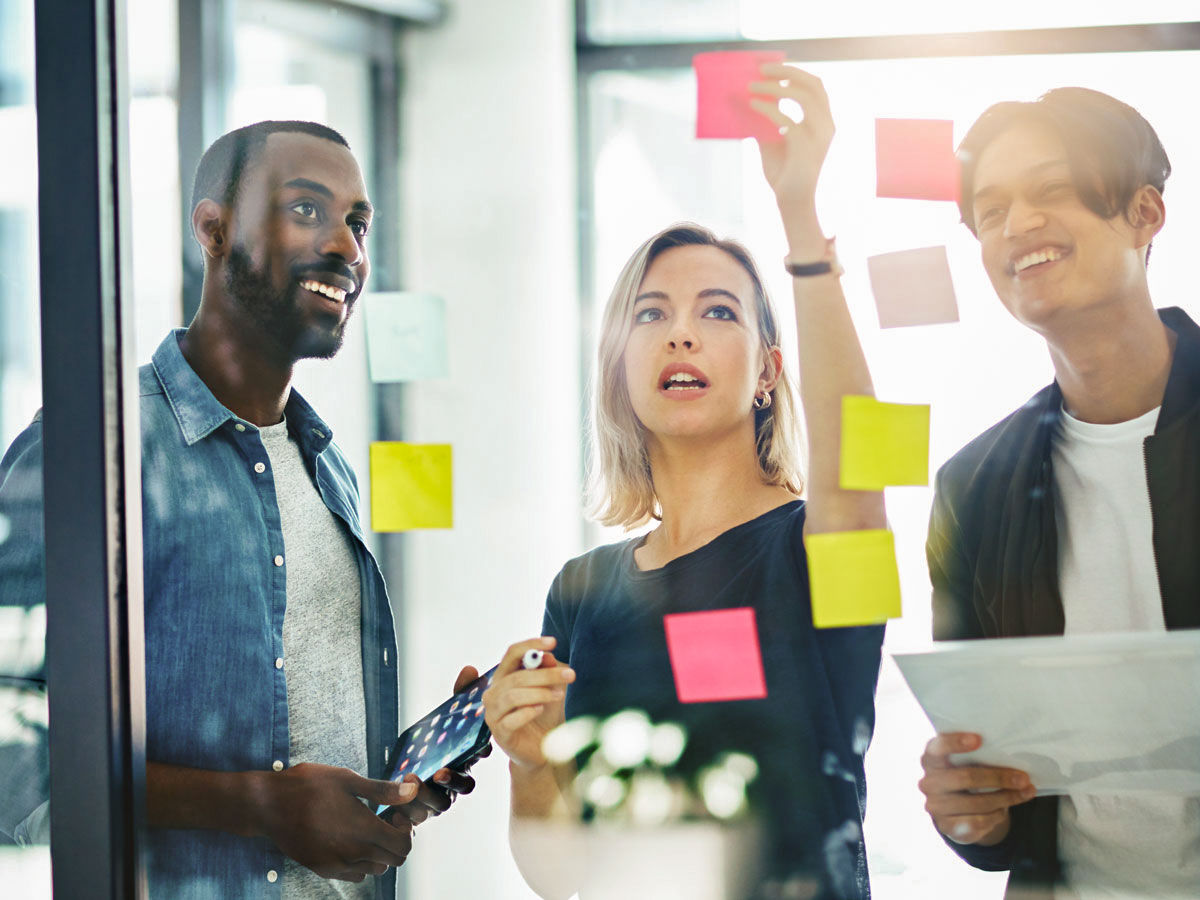 Teamwork, planning and reading sticky notes while brainstorming, talking or sharing ideas. Diverse group of creative businesspeople meeting, training with tablet or paperwork to innovate vision plan