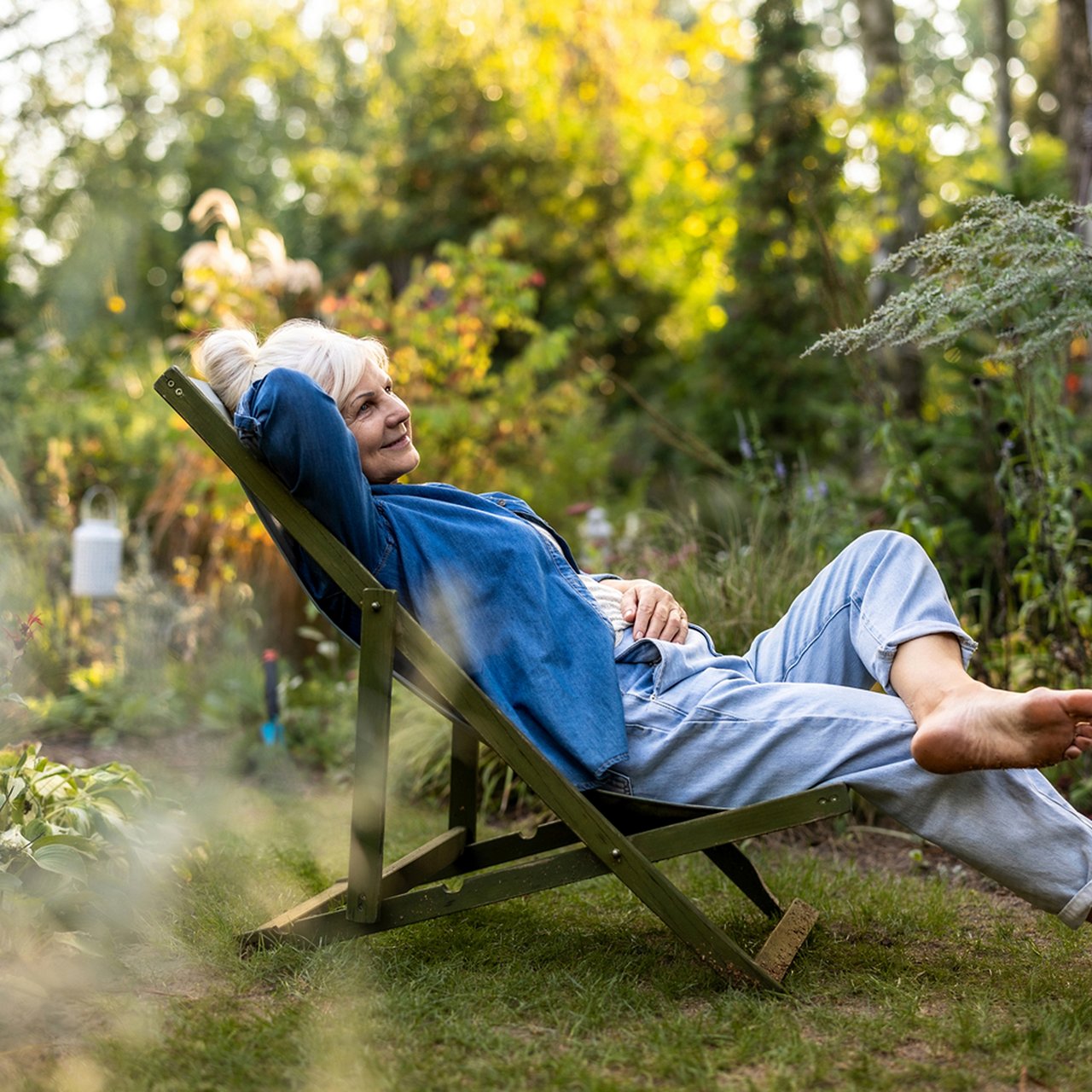 Person relaxing in a deck chair in a sunlit garden.
