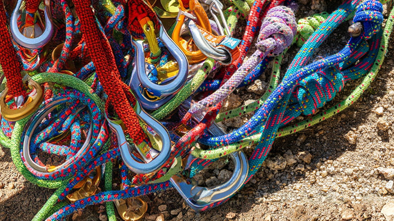 Close-up of colourful climbing ropes and metal carabiners on a gravel surface.