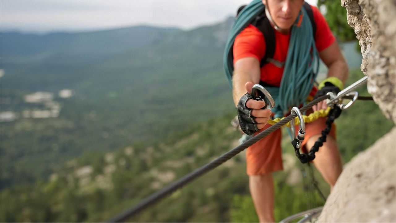 Person using climbing gear on a steep rock face above a mountainous landscape.