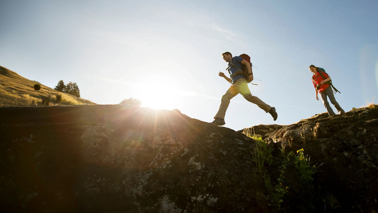 Two hikers on a rocky path, silhouetted against the rising sun.