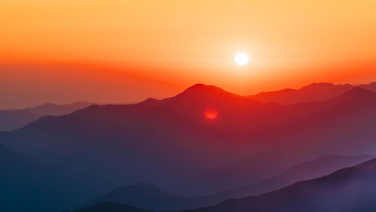 Sunrise or sunset above distant mountain peaks with a gradient orange sky.