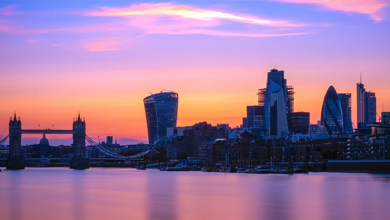 London skyline at sunset with the River Thames, Tower Bridge and modern skyscrapers.