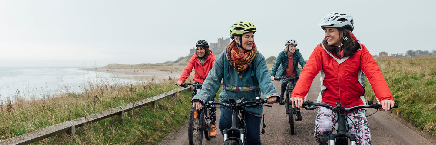 Four cyclists riding along a coastal path beside the beach.