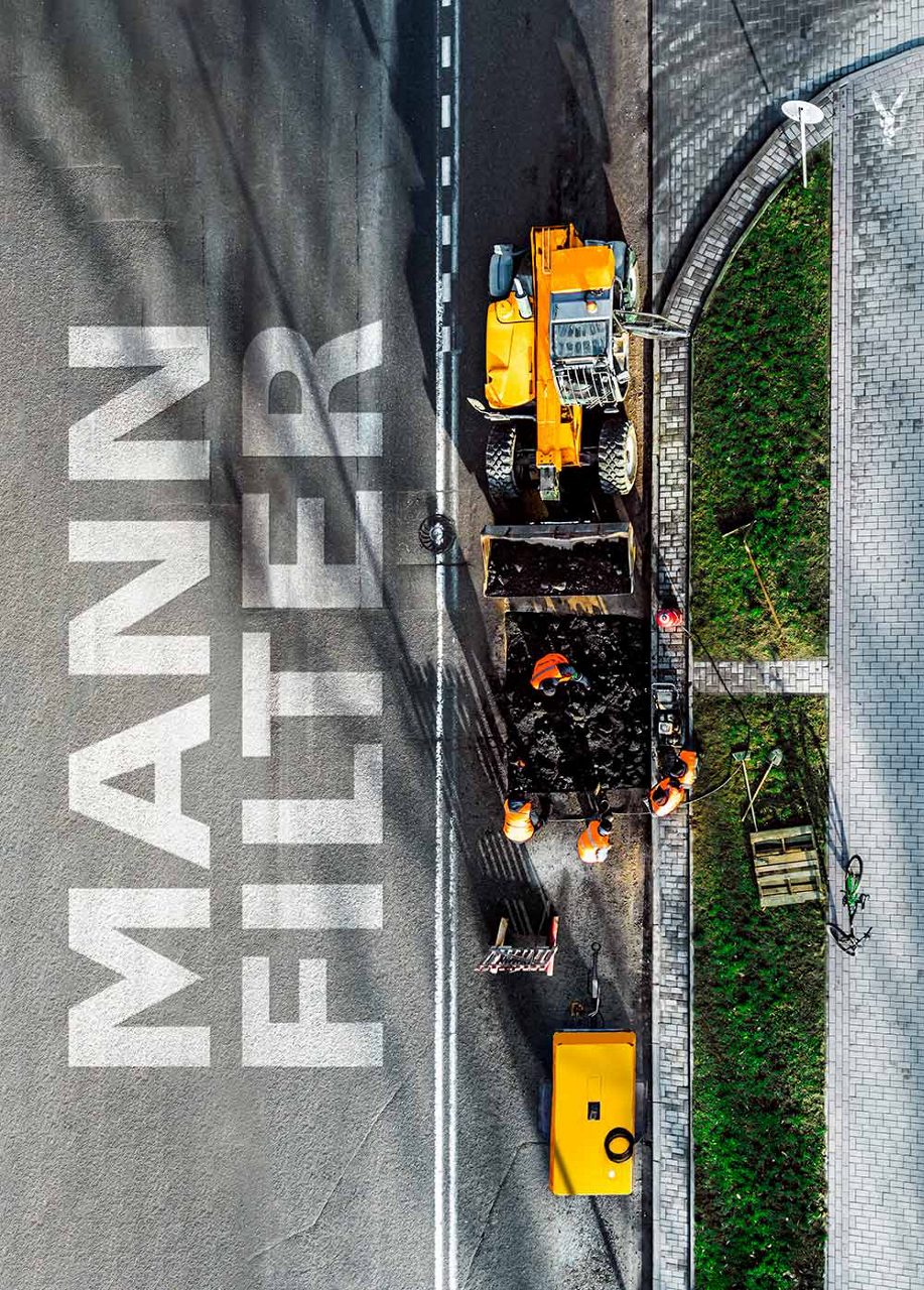 可見車輛與工人的道路施工現場一覽，人行道上有MANN-FILTER商標