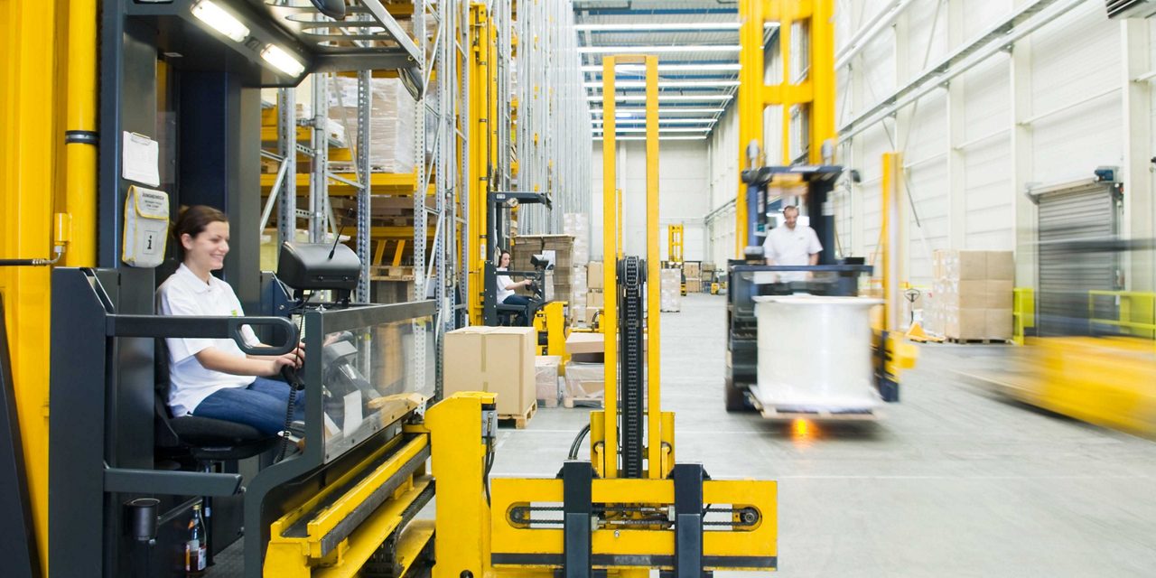 A forklift operating in a warehouse with a worker in the foreground and MANN-FILTER branding