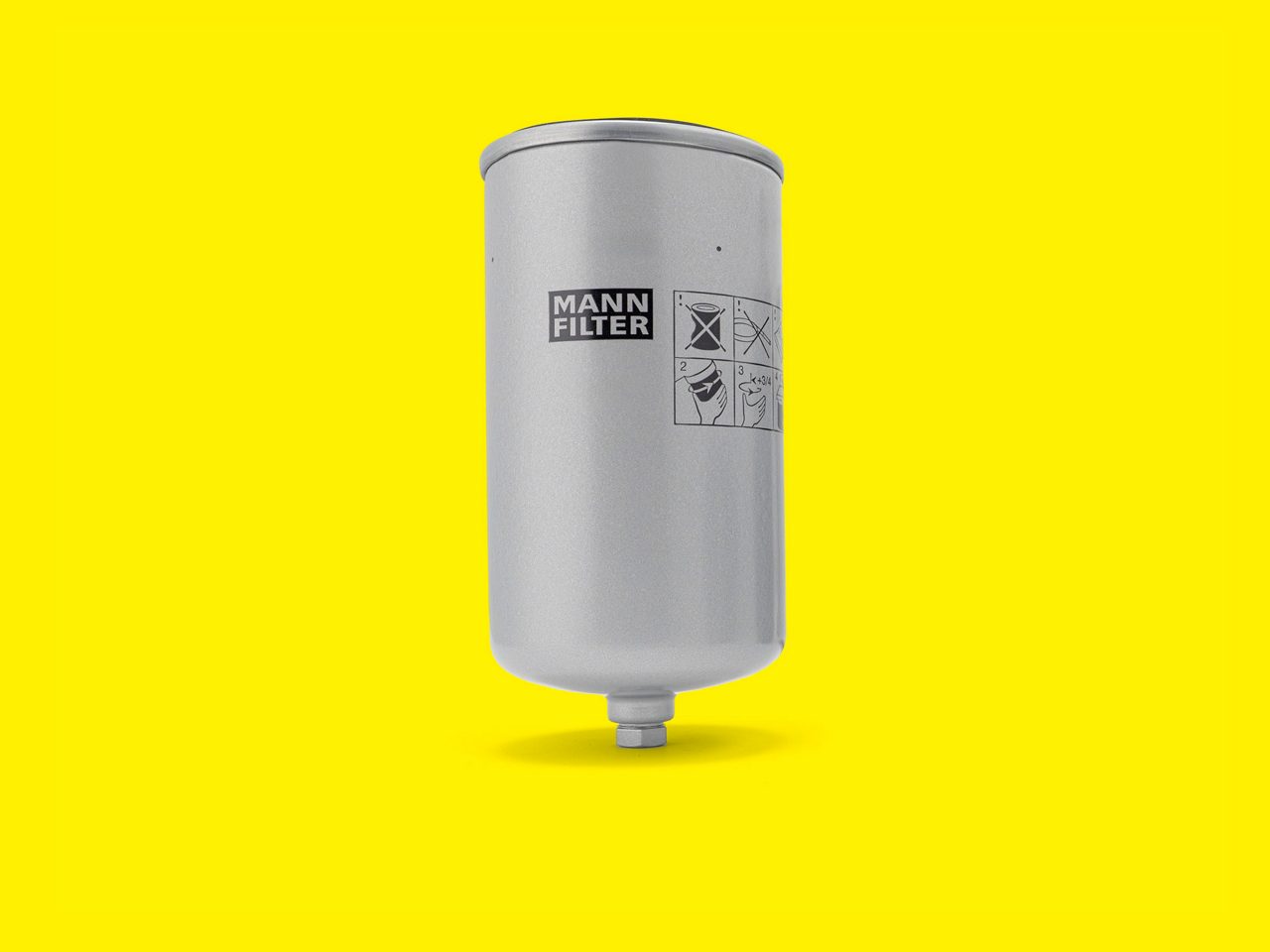 A silver MANN-FILTER fuel filter for industrial engines displayed on a bright yellow background