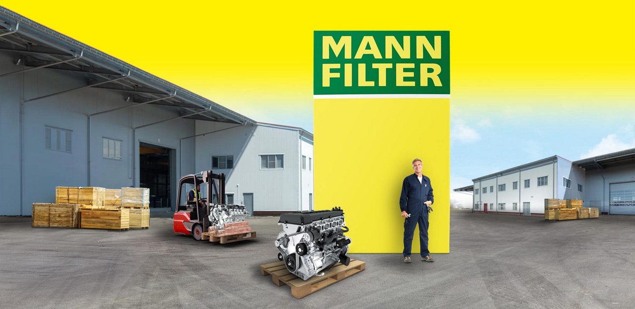 Industrial engine and mechanic in front of a MANN-FILTER box, forklift and warehouse in background