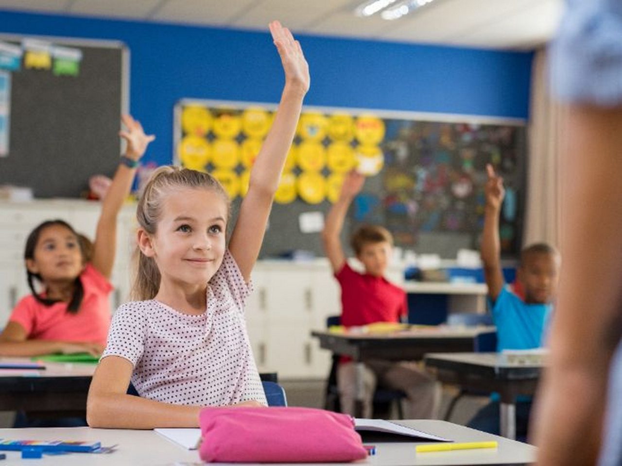 Students in a bright classroom raise their hands. The image is used in the context of modern air filtration solutions aimed at improving indoor air quality in school buildings.