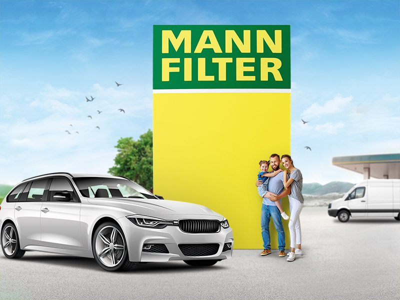 Family standing near a silver passenger car and MANN-FILTER branding with a van and gas station