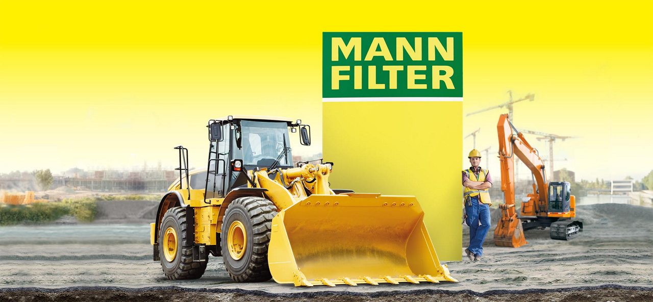Yellow loader and excavator near MANN-FILTER branding with a worker standing in the foreground