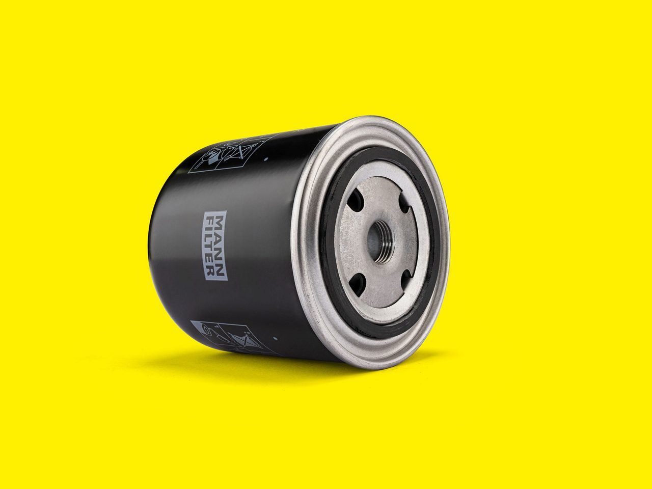 Filtro de refrigerante MANN-FILTER negro con base metálica, sobre fondo amarillo brillante