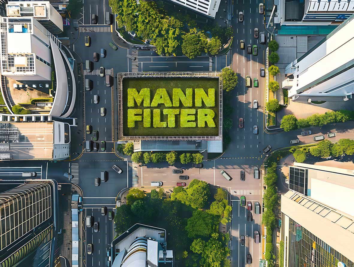 Vista aérea de un cruce urbano con MANN-FILTER sobre un tejado rodeado de coches y transportistas