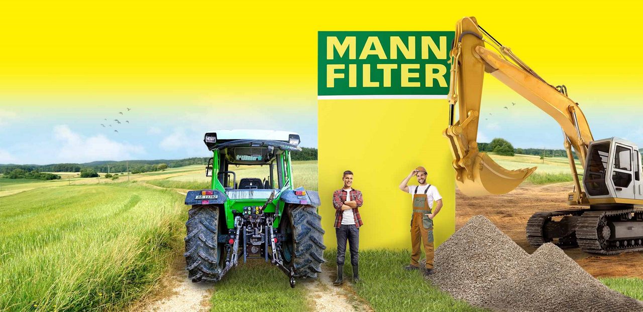 A green tractor, two men, and a yellow excavator in a field with a large MANN-FILTER box