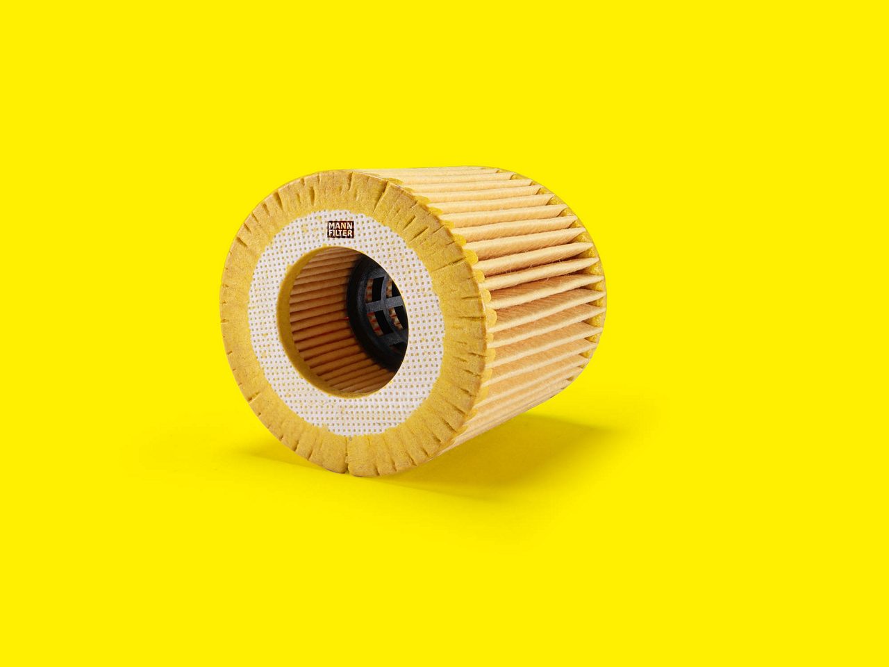 Filtro de aceite MANN-FILTER cilíndrico con diseño plisado sobre fondo amarillo brillante