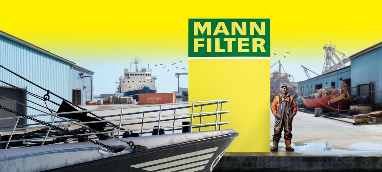 A dockyard scene with boats, a man, and a bright yellow MANN-FILTER logo in the background