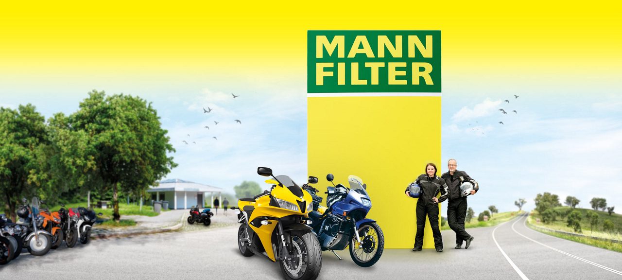 Motorcycles on a road, people standing nearby, and a yellow MANN-FILTER logo in the background