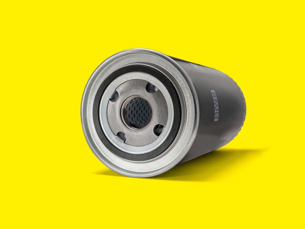 A black and silver oil filter for forklifts displayed horizontally on a bright yellow background