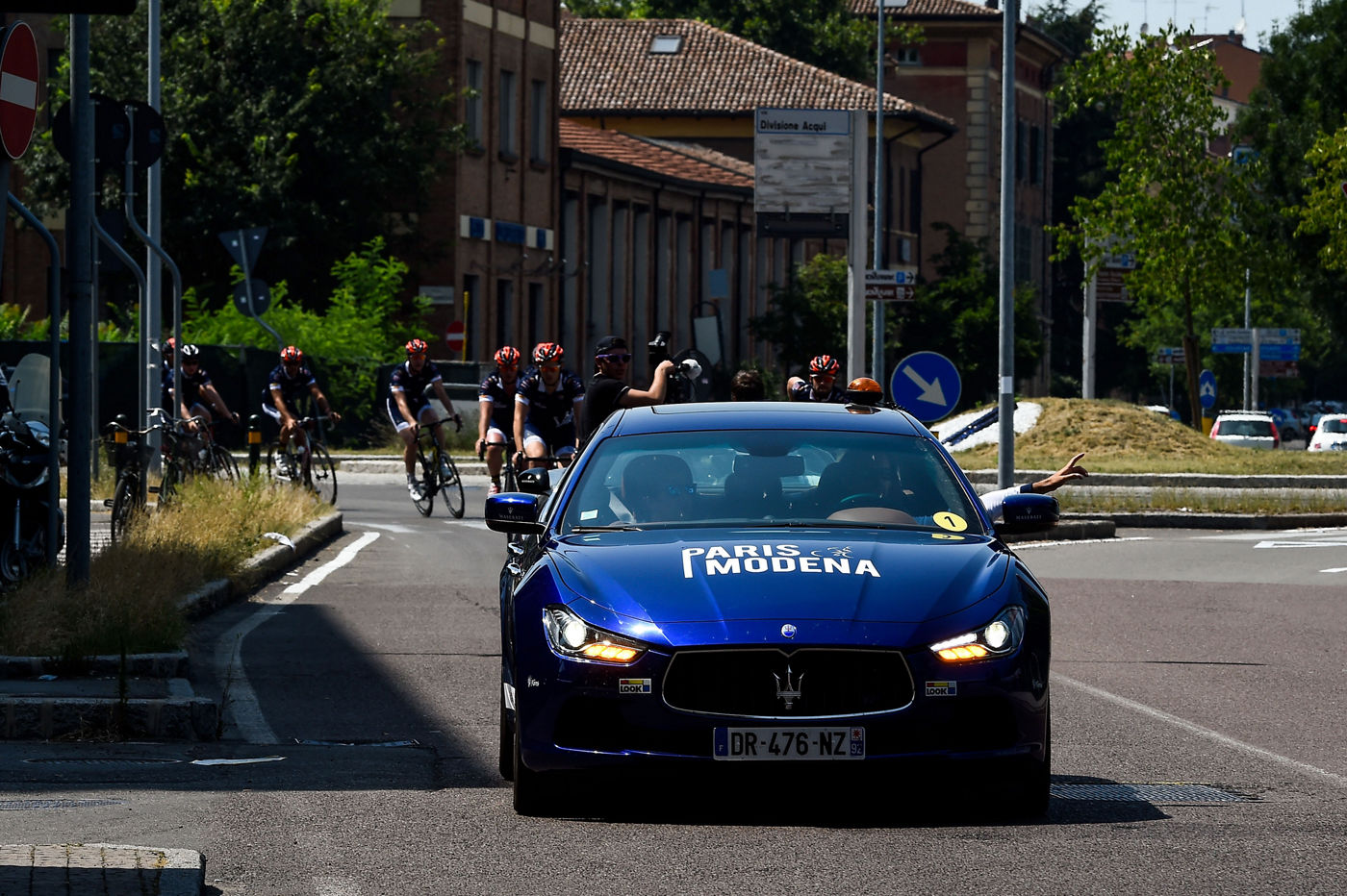 Vehículo delante de ciclistas vestidos con camiseta Maserati para el tour París-Modena en 2016
