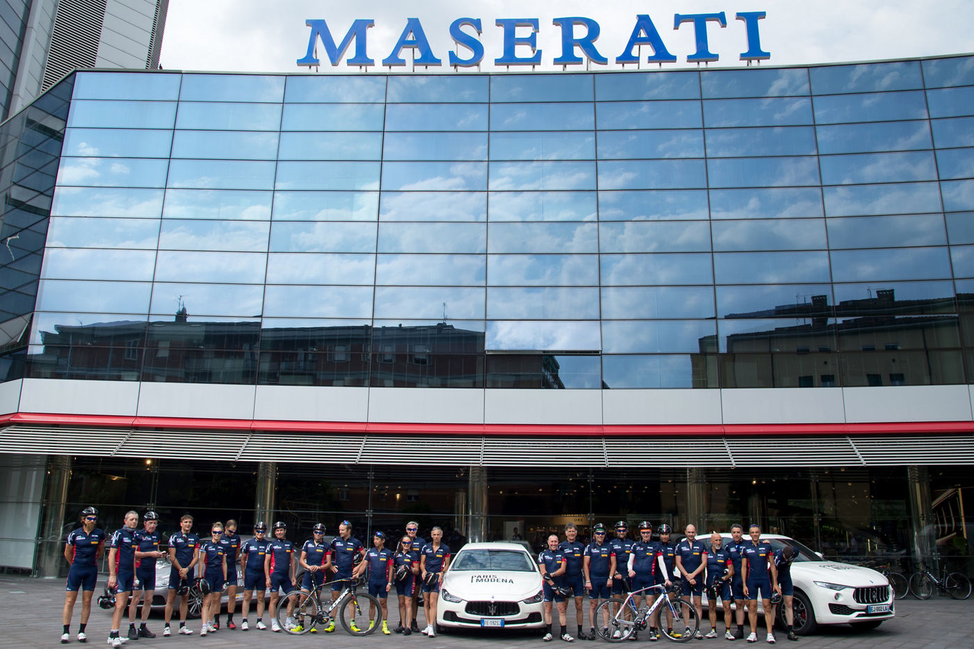 Ciclistas en frente de sede Maserati en Módena con modelos Maserati