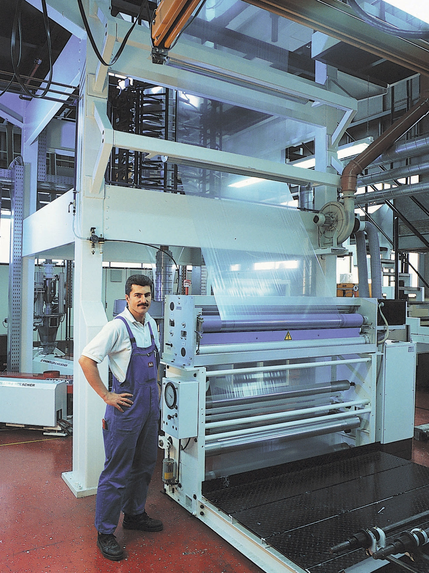 Mitarbeitende Person steht neben einer großen Maschine zur Herstellung transparenter Kunststofffolien in einer Fabrikhalle.