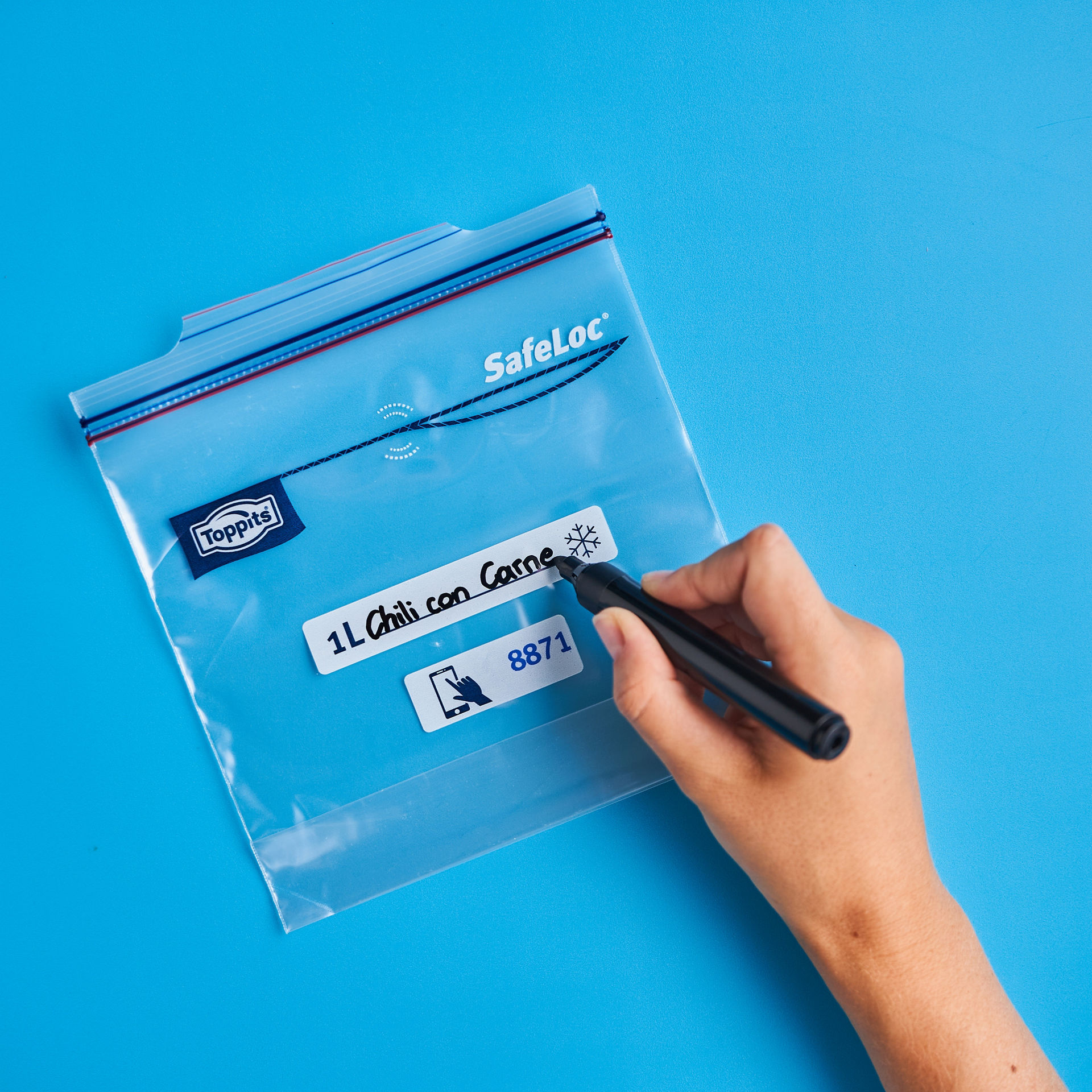 Hand beschriftet mit schwarzem Stift einen Toppits SafeLoc Gefrierbeutel auf blauem Hintergrund 1