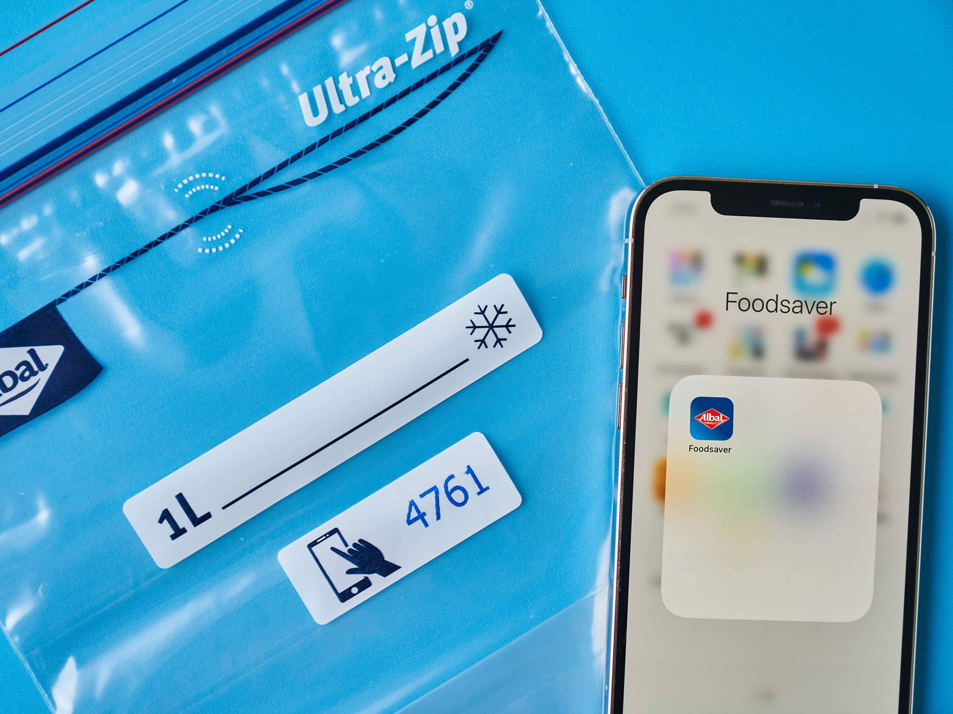 Un smartphone affichant l’application Albal® Foodsaver® est posé à côté d’un sachet UltraZip® sur un fond bleu.
