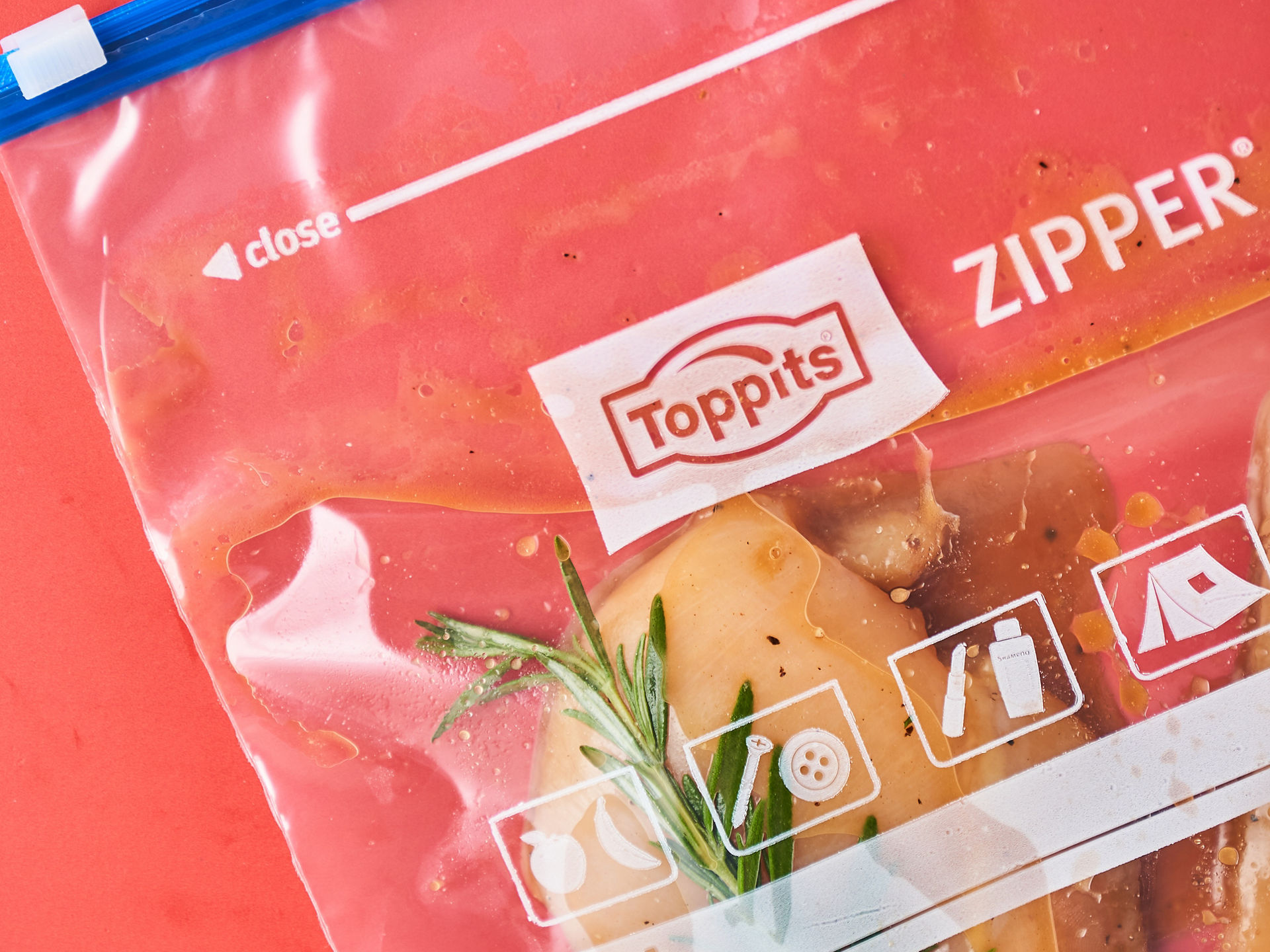 Ein Toppits Zipper Beutel mit mariniertem Hähnchenfleisch und frischem Rosmarin liegt auf einem roten Untergrund. 