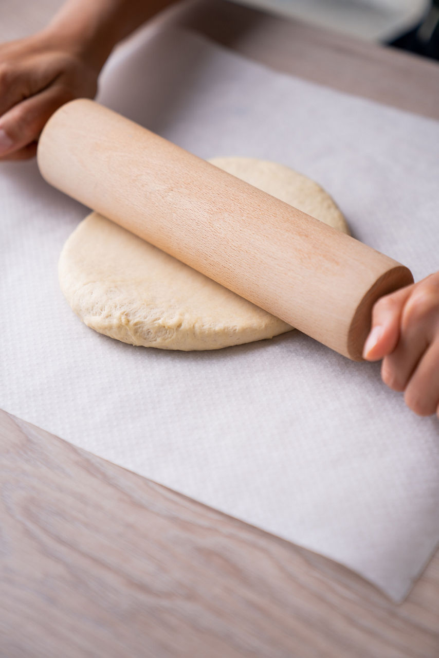 Ein Teig wird mit einem Nudelholz auf Backpapier ausgerollt. 