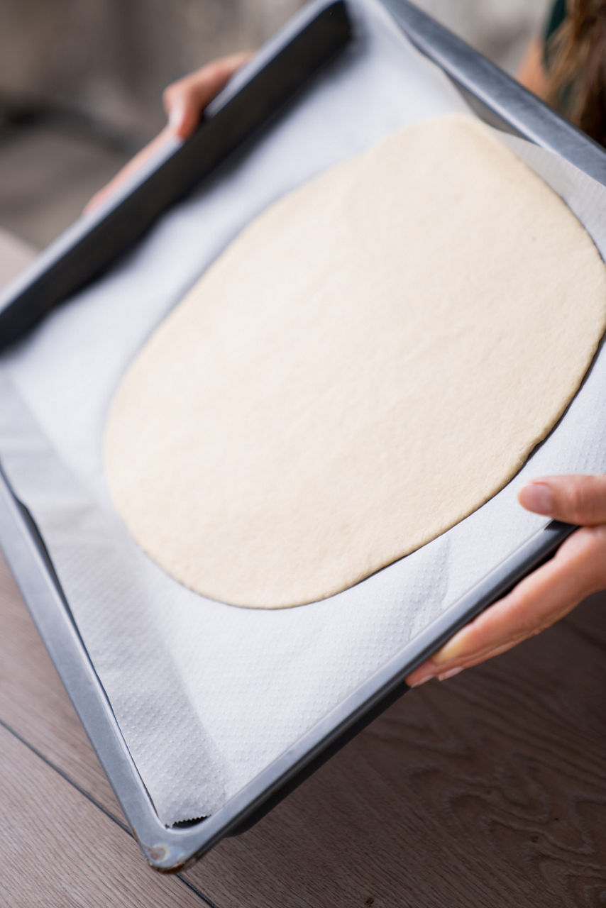 Ein ausgerollter Pizzateig liegt auf Backpapier in einem Backblech. 