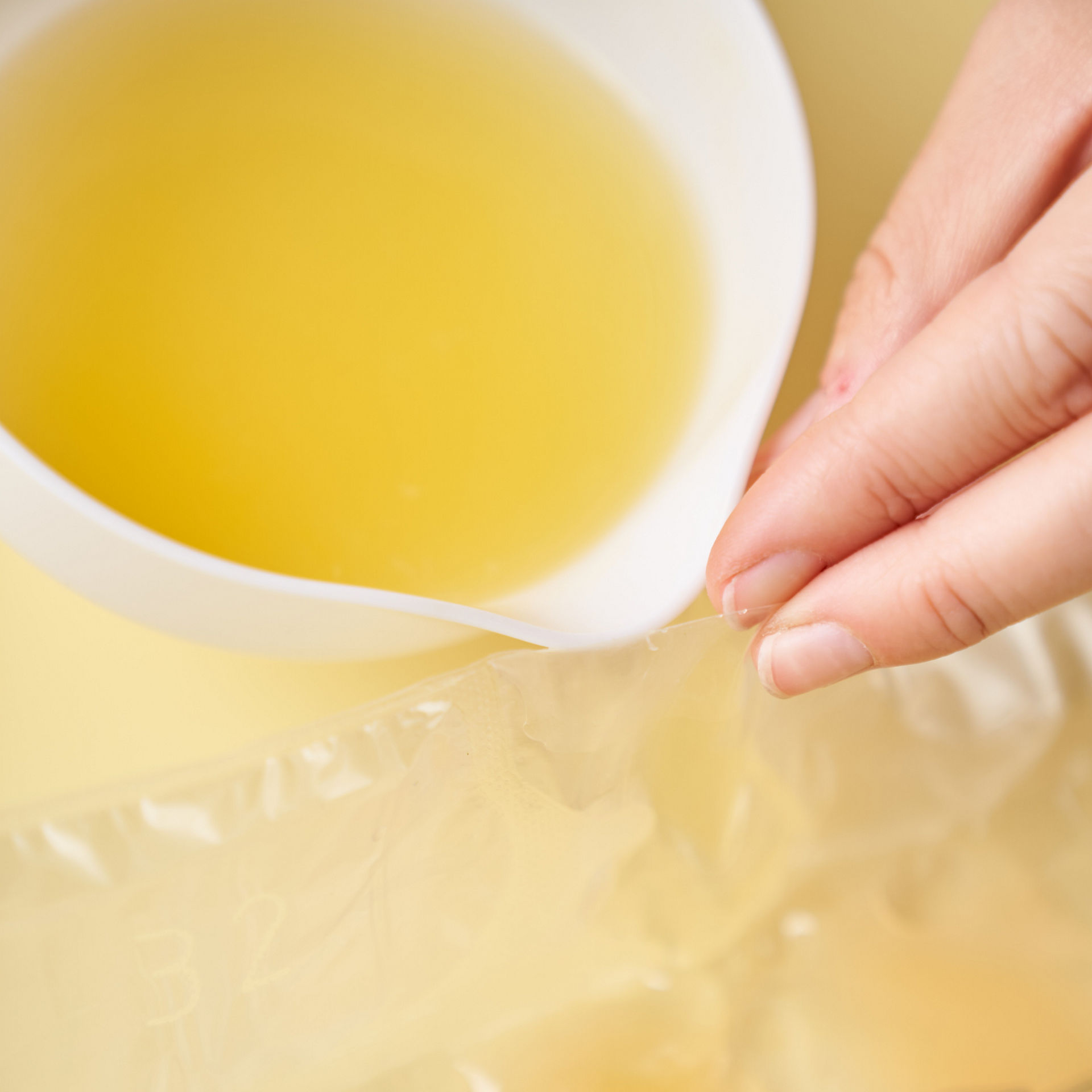 Eine Person gießt Zitronensaft aus einem weißen Messbecher in einen Toppits Eiskugelbeutel. Die Hand hält den Beutel geöffnet, damit der Saft eingefüllt werden kann.