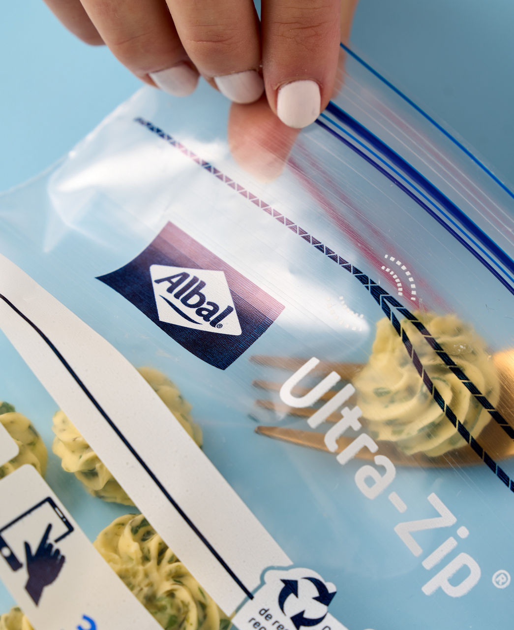 Des mains ferment un sachet de congélation contenant du beurre persillé. 